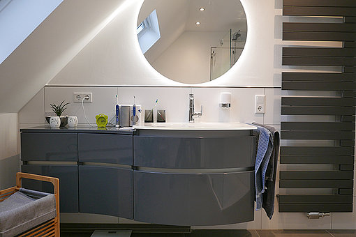 Nach der Sanierung: Grauer Waschtisch mit einem Waschbecken und modernen großen runden Spiegel